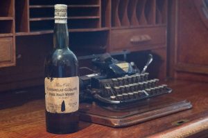 The 1920 bottle of Glenfarclas-Glenlivet Pure Malt Whisky on the desk is actually the youngest thing in the picture. Both the desk and the typewriter predate the whisky.